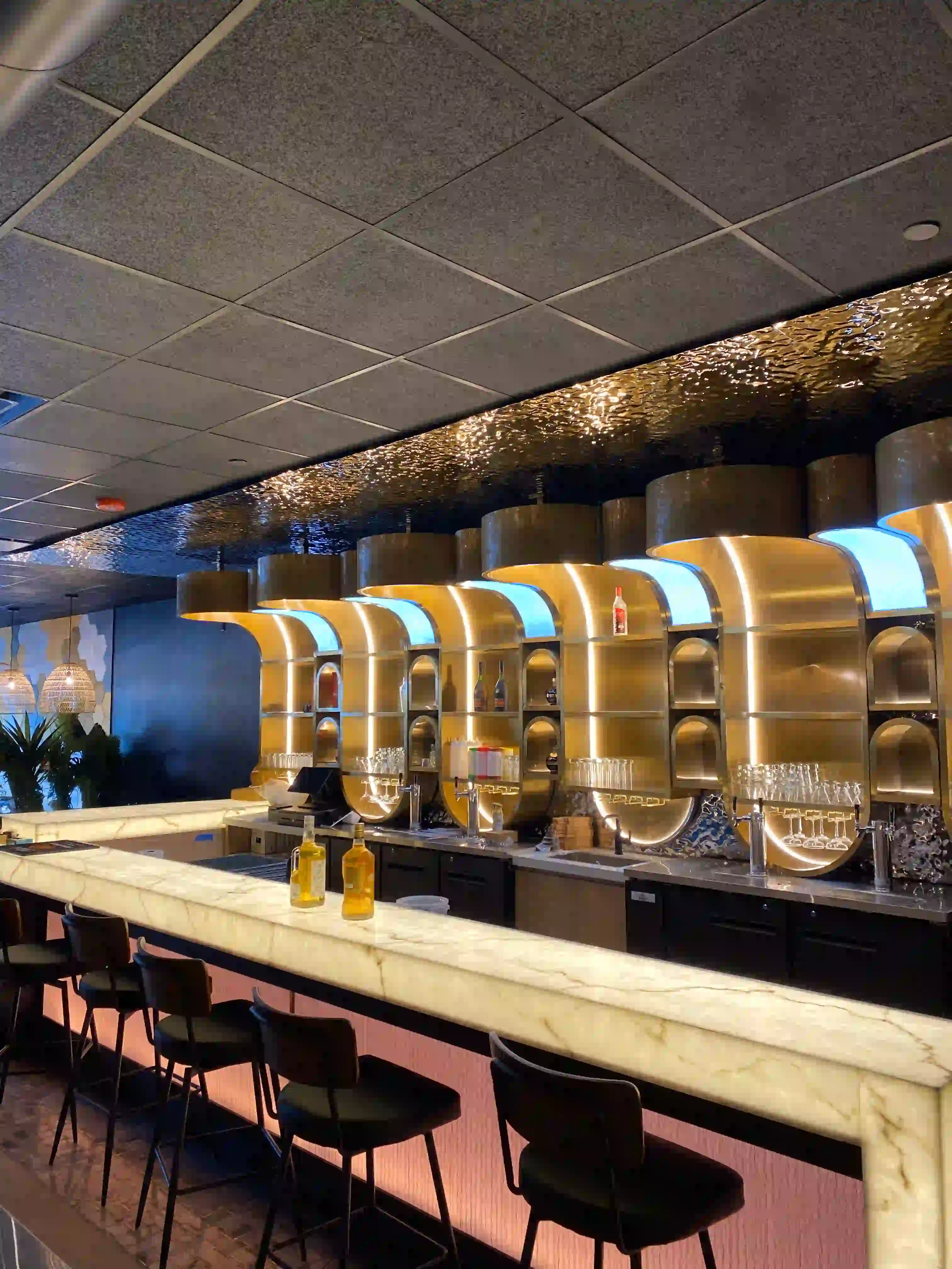 Modern bar interior featuring an illuminated marble counter and curved, gold-paneled back shelving.